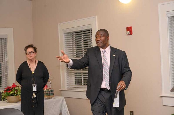 Man speaking to a group. Woman standing in front of a table.